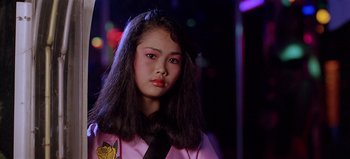 Movie still from “Baraka” (1992), directed by Ron Fricke – A young woman with long black hair wearing a pink shirt; Close Up shot, Low angle