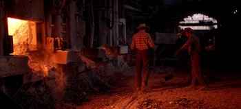 Movie still from “Baraka” (1992), directed by Ron Fricke – A man with a hat and a shovel walking down a dirt road; Wide shot, High angle