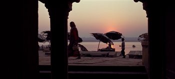 Movie still from “Baraka” (1992), directed by Ron Fricke – People walking on the beach with umbrellas at sunset; Wide shot, Low angle
