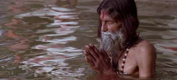 Movie still from “Baraka” (1992), directed by Ron Fricke – An old man with long hair and a long beard is praying in a body of water; Medium shot, High angle
