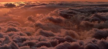 Movie still from “Baraka” (1992), directed by Ron Fricke – The sun is setting above the clouds in the sky; Extreme Wide shot, High angle