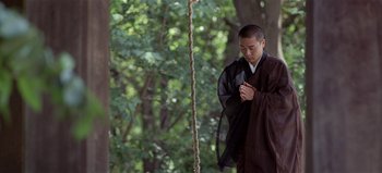 Movie still from “Baraka” (1992), directed by Ron Fricke – A man standing in the woods with his hands clasped together; Medium shot, Low angle