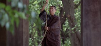 Movie still from “Baraka” (1992), directed by Ron Fricke – A man holding a rope in a forest; Medium shot, Low angle