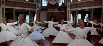 Movie still from “Baraka” (1992), directed by Ron Fricke – A group of men in white robes dancing in a room; Extreme Wide shot, Low angle