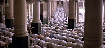 Movie still from “Baraka” (1992), directed by Ron Fricke – A large group of people praying inside of a building; Extreme Wide shot, High angle