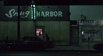 Movie still from “Barfly” (1987), directed by Barbet Schroeder – A car parked on the side of the road in front of a building; Extreme Wide shot, Low angle