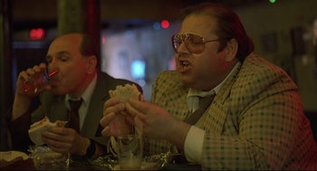 Movie still from “Barfly” (1987), directed by Barbet Schroeder – A man sitting at a table with a sandwich in front of him; Medium shot, Over the shoulder angle