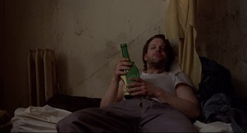Movie still from “Barfly” (1987), directed by Barbet Schroeder – A man sitting on a bed holding a bottle of beer; Close Up shot, High angle