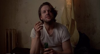 Movie still from “Barfly” (1987), directed by Barbet Schroeder – A man sitting on the floor holding a bottle of beer; Close Up shot, Low angle