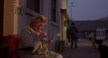 Movie still from “Barfly” (1987), directed by Barbet Schroeder – An older woman sitting on the side of the street reading; Medium shot, Low angle