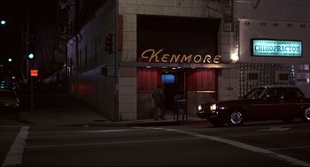 Movie still from “Barfly” (1987), directed by Barbet Schroeder – A car parked on the side of the road next to a building; Extreme Wide shot, High angle