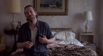 Movie still from “Barfly” (1987), directed by Barbet Schroeder – A man sitting on a bed holding a cell phone; Medium shot, High angle