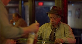 Movie still from “Barfly” (1987), directed by Barbet Schroeder – An older man sitting at a table with a cigarette in his hand; Medium shot, Over the shoulder angle