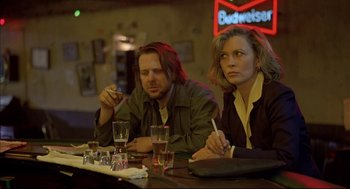 Movie still from “Barfly” (1987), directed by Barbet Schroeder – A man and a woman sitting at a table with drinks; Medium shot, Low angle