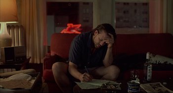 Movie still from “Barfly” (1987), directed by Barbet Schroeder – A man sitting on a couch writing on a piece of paper; Medium shot, High angle
