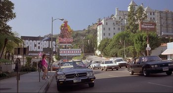 Movie still from “Barfly” (1987), directed by Barbet Schroeder – A busy city street with cars parked on the side of the road; Extreme Wide shot, Low angle