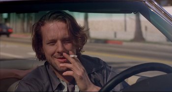Movie still from “Barfly” (1987), directed by Barbet Schroeder – A man sitting in the drivers seat of a car while smoking a cigarette; Close Up shot, Low angle