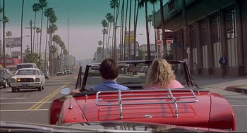 Movie still from “Barfly” (1987), directed by Barbet Schroeder – A man and a woman riding in the back of a red car down a street; Wide shot, High angle