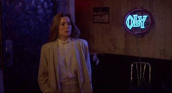 Movie still from “Barfly” (1987), directed by Barbet Schroeder – A woman standing in a room with a neon sign in the background; Medium shot, Over the shoulder angle