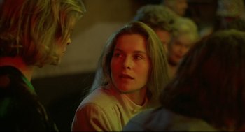Movie still from “Barfly” (1987), directed by Barbet Schroeder – A woman with long blonde hair sitting next to a group of people; Close Up shot, Over the shoulder angle