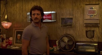 Movie still from “Barfly” (1987), directed by Barbet Schroeder – A man standing next to a fan in a room; Medium shot, Low angle