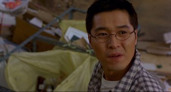 Movie still from “Barking Dogs Never Bite” (2000), directed by Bong Joon Ho – A person wearing glasses and a plaid shirt; Close Up shot, Over the shoulder angle