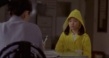 Movie still from “Barking Dogs Never Bite” (2000), directed by Bong Joon Ho – A girl in a yellow raincoat sitting at a table; Medium shot, Over the shoulder angle