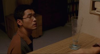 Movie still from “Barking Dogs Never Bite” (2000), directed by Bong Joon Ho – A man sitting at a wooden table with a glass of water; Close Up shot, High angle