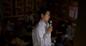 Movie still from “Barking Dogs Never Bite” (2000), directed by Bong Joon Ho – A man holding a microphone in his hands; Medium shot, Low angle