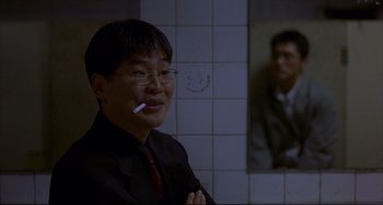 Movie still from “Barking Dogs Never Bite” (2000), directed by Bong Joon Ho – A man smoking a cigarette in front of a mirror; Medium shot, Over the shoulder angle