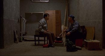 Movie still from “Barking Dogs Never Bite” (2000), directed by Bong Joon Ho – Two men sitting on a chair in an empty room; Wide shot, High angle