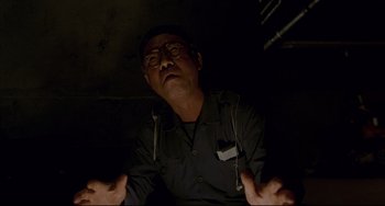 Movie still from “Barking Dogs Never Bite” (2000), directed by Bong Joon Ho – An older man with glasses is sitting in a dark room; Close Up shot, Low angle