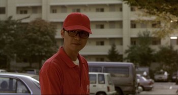 Movie still from “Barking Dogs Never Bite” (2000), directed by Bong Joon Ho – A man in a red shirt and a red hat; Close Up shot, Low angle