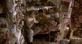 Movie still from “Barking Dogs Never Bite” (2000), directed by Bong Joon Ho – Two people sitting in a store eating food; Wide shot, High angle