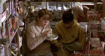Movie still from “Barking Dogs Never Bite” (2000), directed by Bong Joon Ho – A woman and a boy eating noodles on a plate; Medium shot, Overhead angle