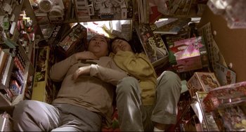 Movie still from “Barking Dogs Never Bite” (2000), directed by Bong Joon Ho – A couple of people laying on top of a pile of books; Medium shot, Overhead angle