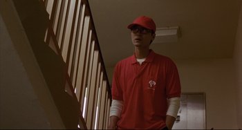 Movie still from “Barking Dogs Never Bite” (2000), directed by Bong Joon Ho – A man in a red shirt and a red hat standing next to a railing; Medium shot, Low angle