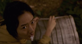 Movie still from “Barking Dogs Never Bite” (2000), directed by Bong Joon Ho – A woman with a flower in her mouth sitting on a bench; Close Up shot, High angle