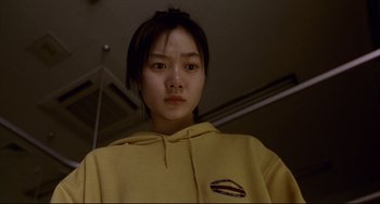 Movie still from “Barking Dogs Never Bite” (2000), directed by Bong Joon Ho – A young woman in a yellow hoodie is looking at the camera; Close Up shot, Low angle