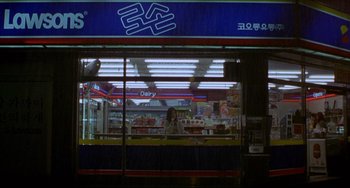 Movie still from “Barking Dogs Never Bite” (2000), directed by Bong Joon Ho – A woman standing in front of a dairy store; Wide shot, High angle