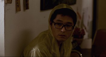 Movie still from “Barking Dogs Never Bite” (2000), directed by Bong Joon Ho – A man wearing a yellow raincoat and glasses; Close Up shot, High angle