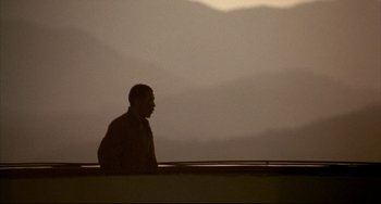 Movie still from “Barking Dogs Never Bite” (2000), directed by Bong Joon Ho – A man standing in front of a window with mountains in the background; Wide shot, Low angle