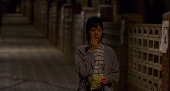 Movie still from “Barking Dogs Never Bite” (2000), directed by Bong Joon Ho – A woman standing on a sidewalk eating food; Medium shot, High angle