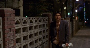 Movie still from “Barking Dogs Never Bite” (2000), directed by Bong Joon Ho – A man standing next to a brick wall at night; Medium shot, Low angle