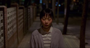 Movie still from “Barking Dogs Never Bite” (2000), directed by Bong Joon Ho – A young asian woman standing in a dark alley way; Medium shot, High angle