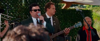Movie still from “Step Brothers” (2008), directed by Adam McKay – A man in a suit and tie holding a microphone and a man in a suit and tie holding a guitar; Medium shot, Over the shoulder angle
