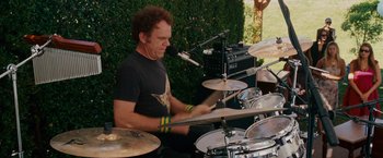 Movie still from “Step Brothers” (2008), directed by Adam McKay – A man playing drums in front of a microphone; Medium shot, Over the shoulder angle