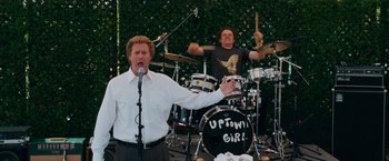 Movie still from “Step Brothers” (2008), directed by Adam McKay – A man singing into a microphone in front of another man playing drums; Medium shot, Low angle