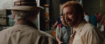 Movie still from “Barney's Version” (2010), directed by Richard J. Lewis – A man in a hat and a tie standing in front of other men; Close Up shot, Over the shoulder angle