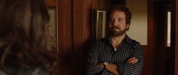 Movie still from “Barney's Version” (2010), directed by Richard J. Lewis – A man standing in a room with his arms crossed; Medium shot, Over the shoulder angle